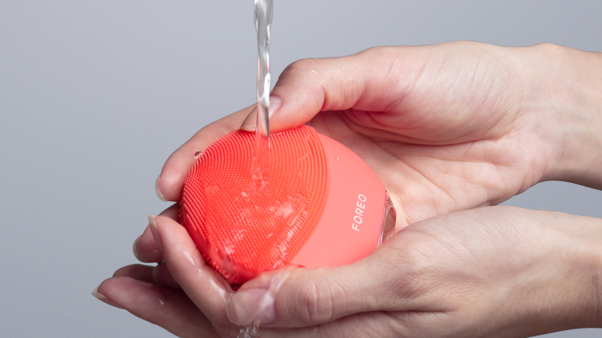 Hands washing FOREO LUNA 4 mini facial cleansing device in coral color