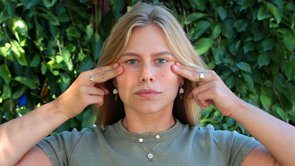A model doing face yoga with fingertips on her cheekbones