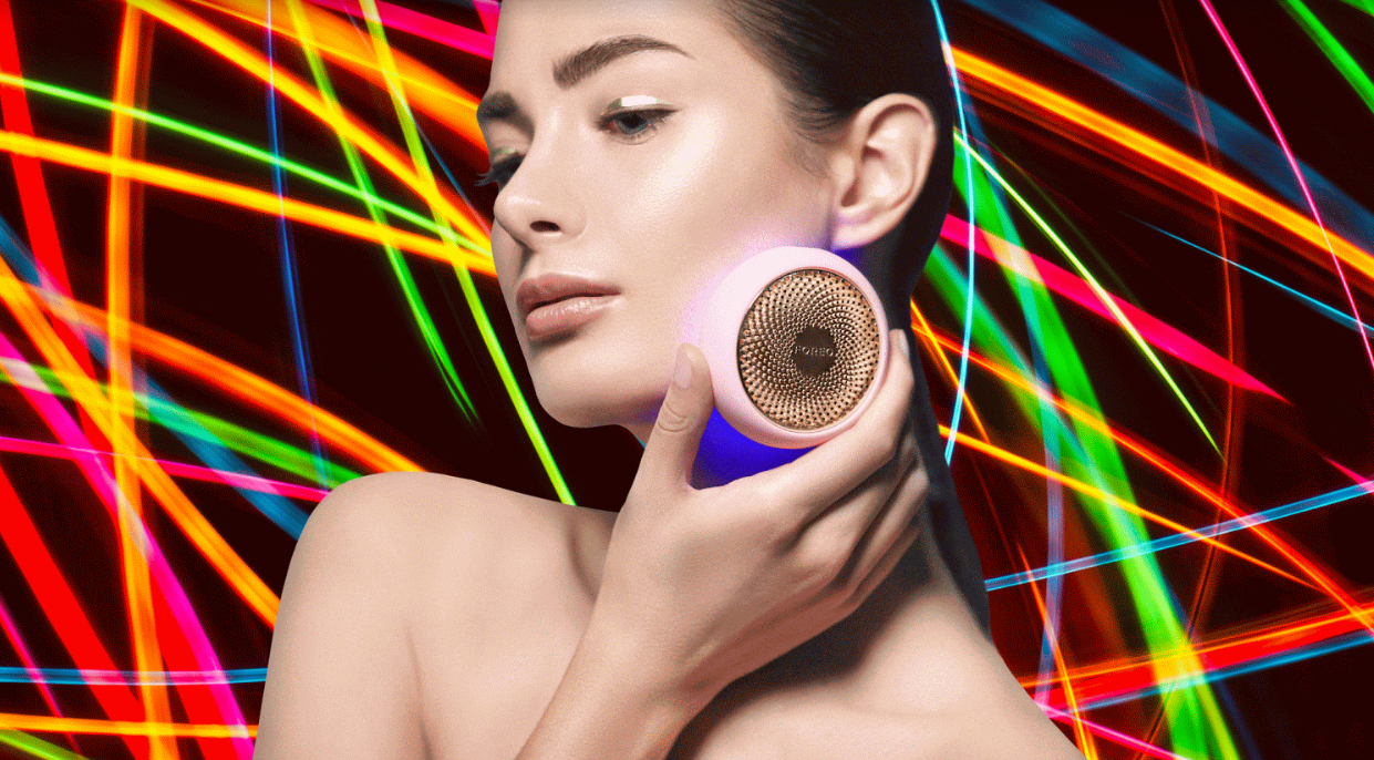 A model holding FOREO UFO device pressed to her face, colorful light rays in the background