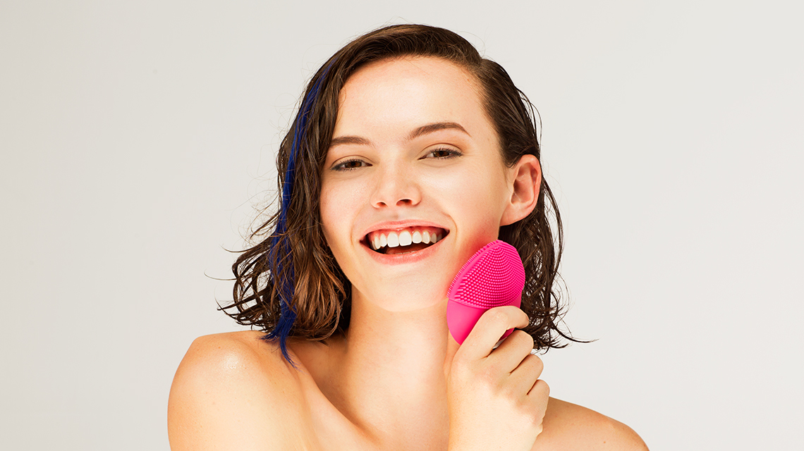 Happy girl holding FOREO LUNA facial cleansing brush on white background