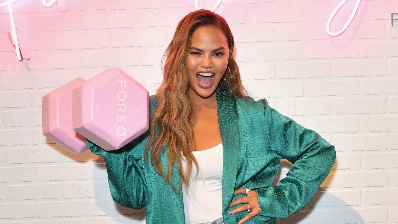 Chrissy Teigen cheekily smiling and lifting a FOREO weight