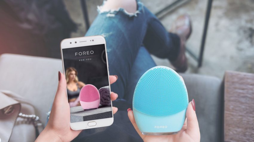 girl holding blue LUNA 3 and phone with FOREO app in the hands