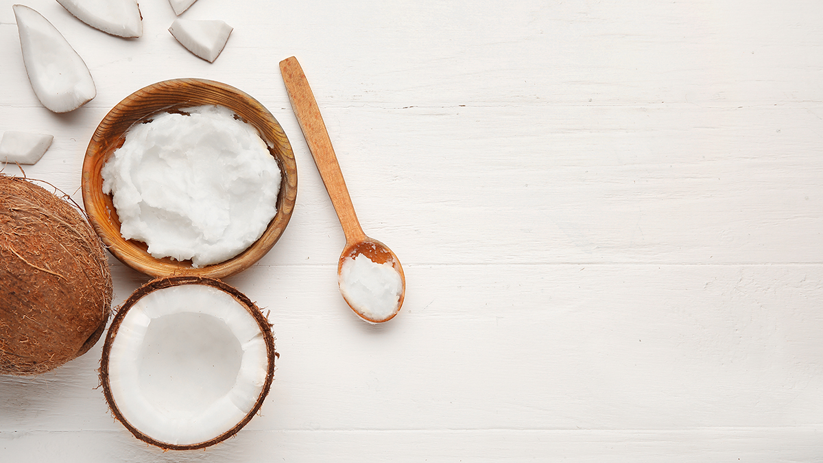 Flatlay of a halved coconut, a wooden bowl witt coconut oil and a wooden spoon with coconut oil