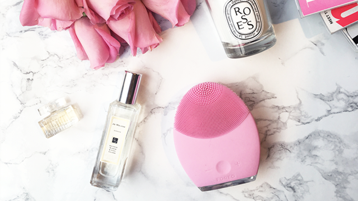 FOREO LUNA™2 on a table with a candle, flowers, and a perfume