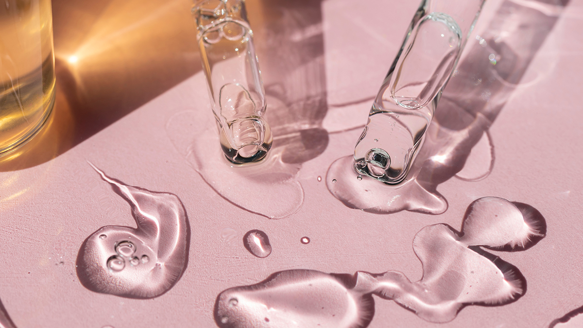 Detail of two pipettes dropping liquid on a pink surface