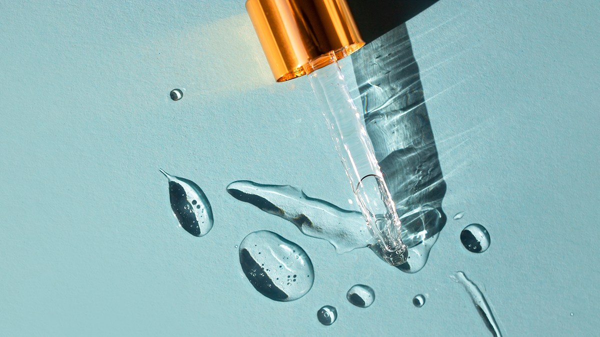 A close up of a glass dropper of serum on blue surface