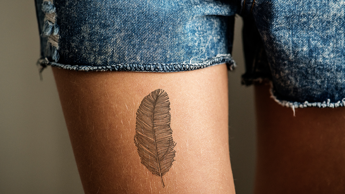 Closeup of a thigh with a feather tattoo