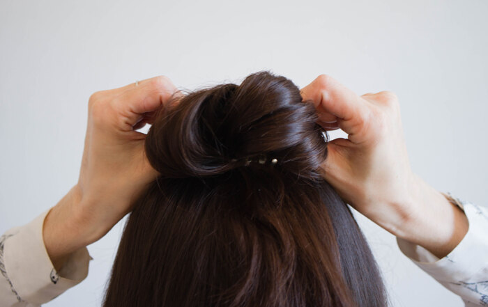 A woman with brown hair ties her hair into a bun