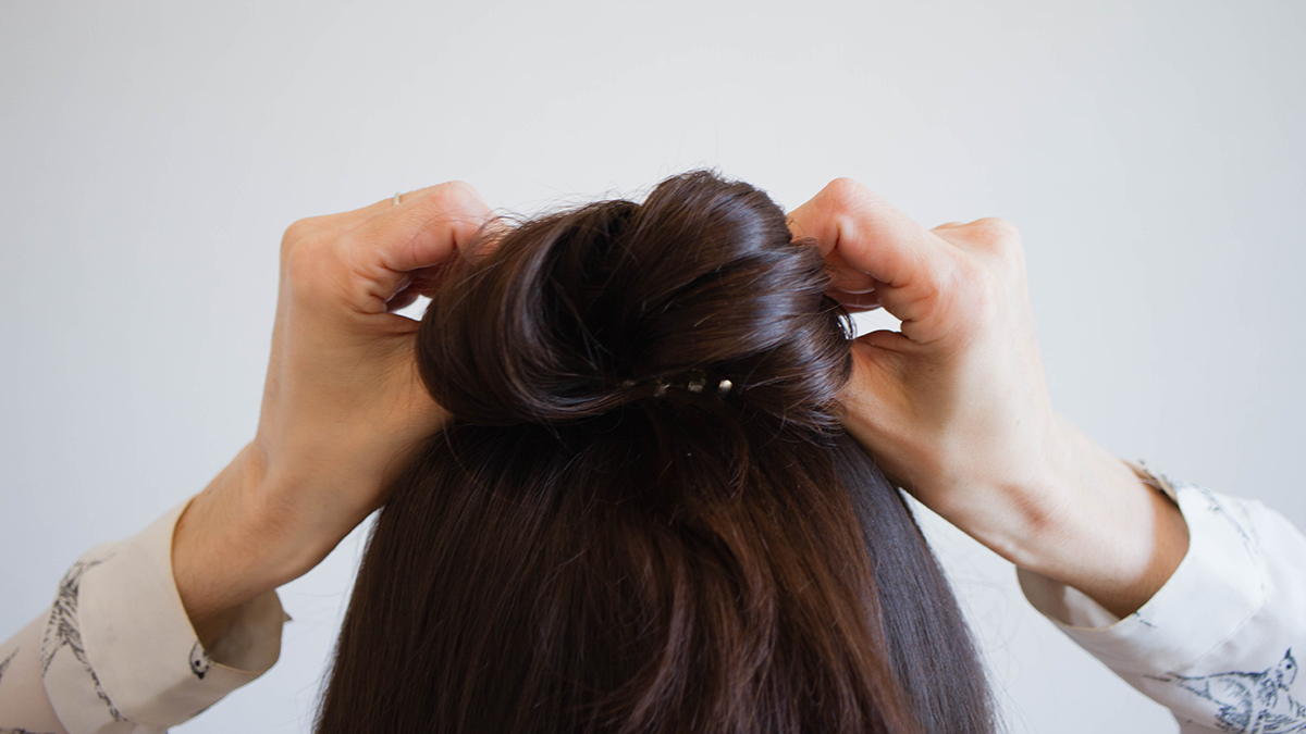 A woman with brown hair ties her hair into a bun