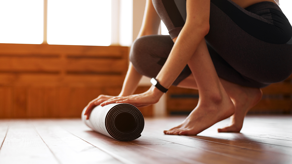 A closeup of a woman's hands and feet rolling out the yoga mat on wooden floor