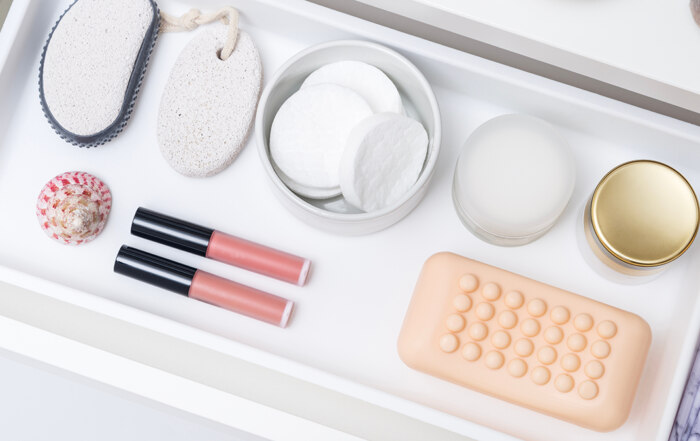 A cosmetic drawer with neatly organized soap, creams, cotton pads, pumice stone, pink lip gloss, and a sea shell