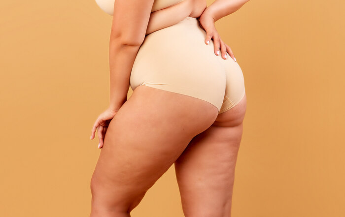 Plus-size model in neutral underwear photographed from the back, on ochre surface