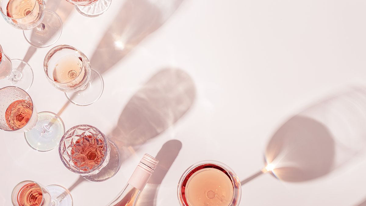 Assortment of wine glasses filled with rose, along with a bottle of rose on a surface where shadows and light play
