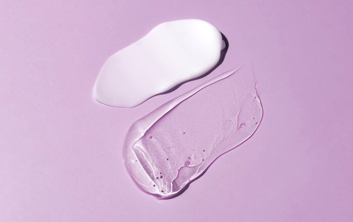 A white and a transparent cosmetic smears on purple background
